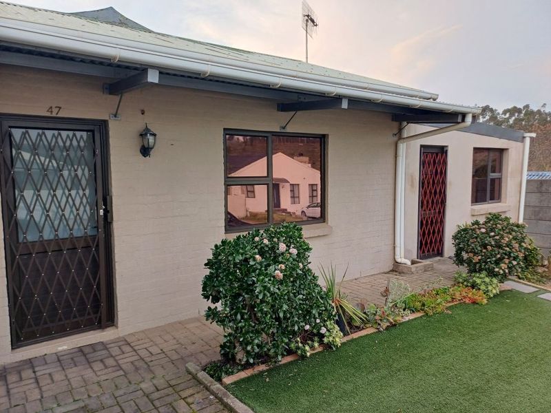 Front elevation of a single-story residence featuring paved walkways, security gates, and aluminium window frames with a small landscaped garden area.