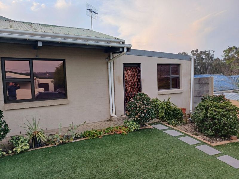 Rear exterior view of the property featuring a corrugated metal roof, aluminium window frames, security gate, paved walkway, and artificial lawn area.