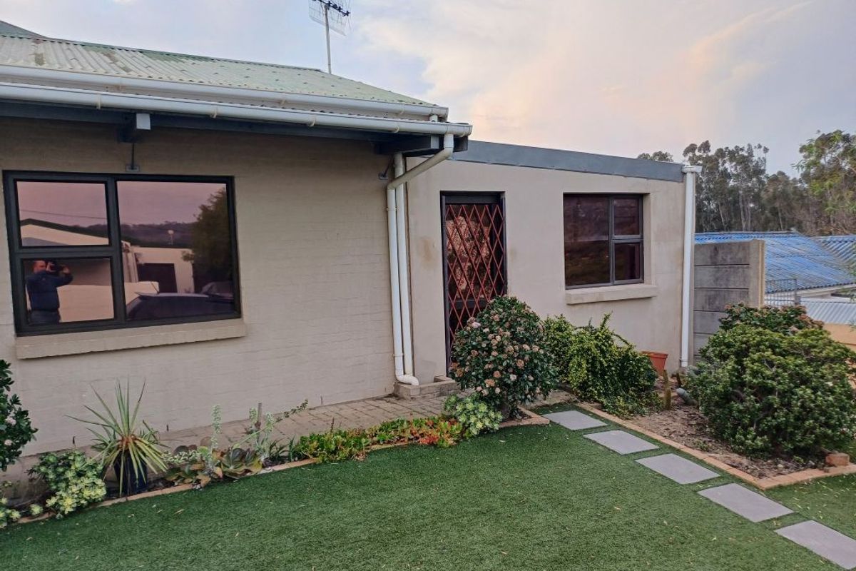 Rear exterior view of the property featuring a corrugated metal roof, aluminium window frames, security gate, paved walkway, and artificial lawn area.