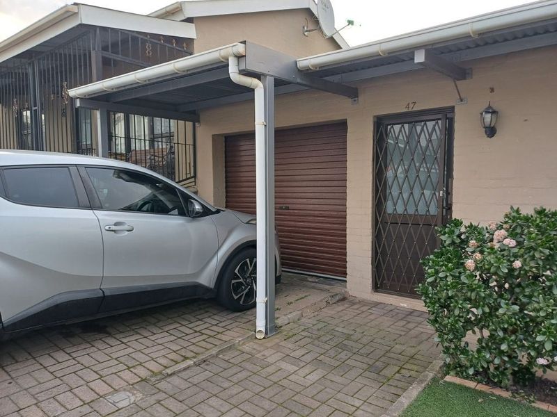 Front exterior view featuring a covered carport, single garage door, and secure entrance with a metal security gate and paved driveway.