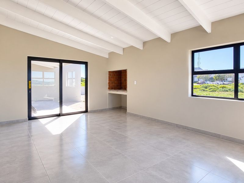 Spacious open-plan living area featuring exposed beam ceilings, tiled flooring, and a built-in indoor braai with direct access to the patio.
