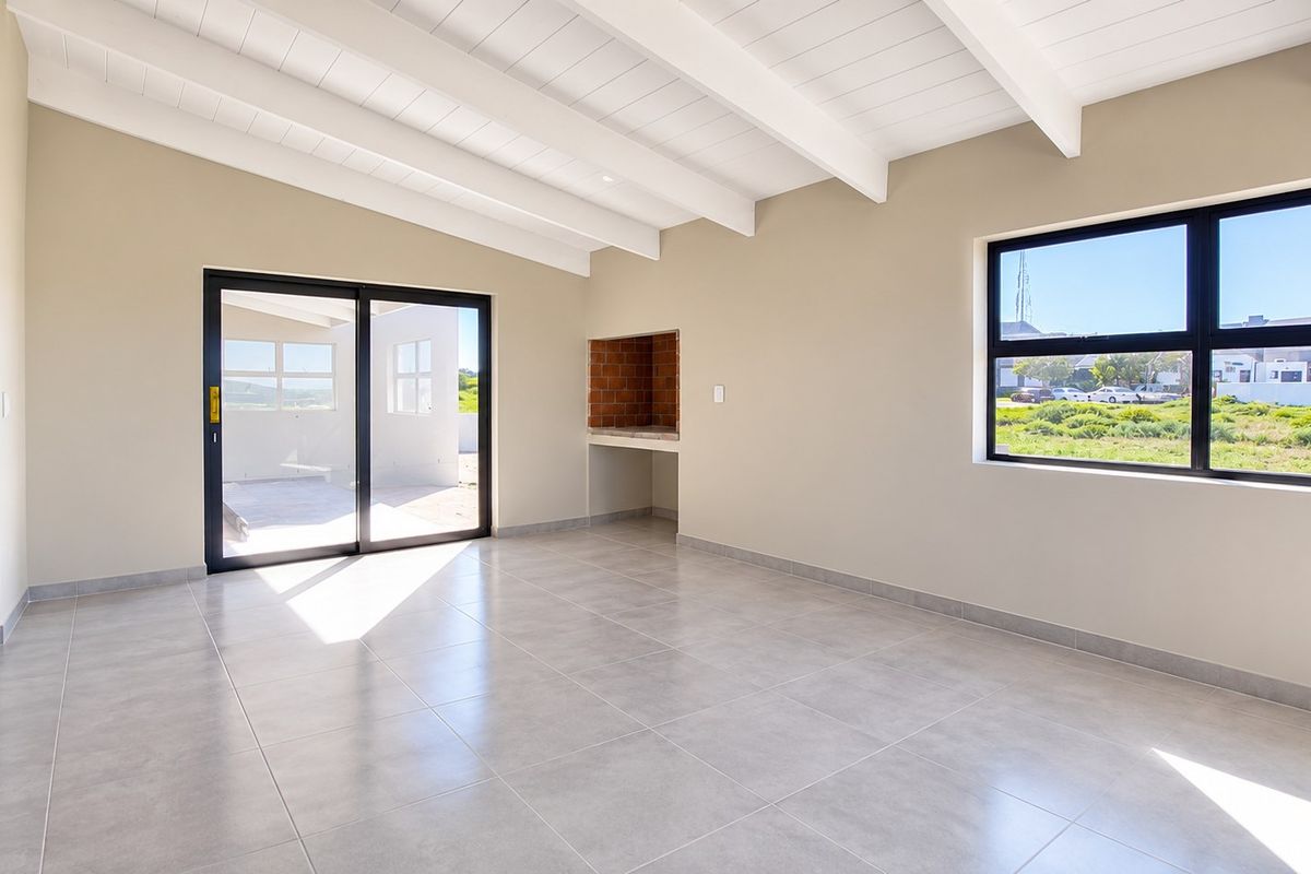 Spacious open-plan living area featuring exposed beam ceilings, tiled flooring, and a built-in indoor braai with direct access to the patio.