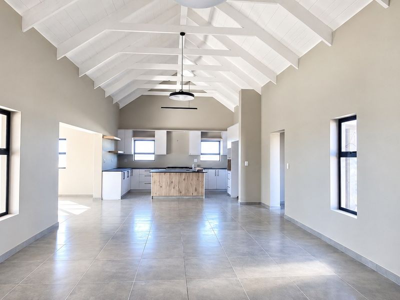 Spacious open-plan living and kitchen area featuring a high vaulted ceiling with exposed trusses, modern tiled flooring, and a central kitchen island.