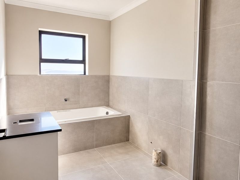 Modern bathroom featuring a built-in bathtub, neutral wall tiles, and a vanity cabinet with a stone countertop.