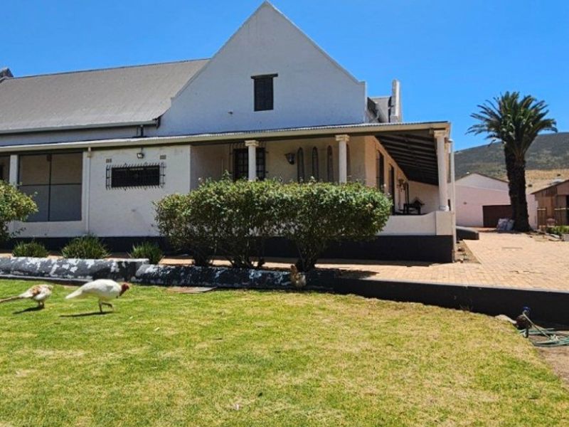 Rear view of a traditional farmhouse featuring a covered patio, gabled roof architecture, and a spacious garden area with an adjacent outbuilding.