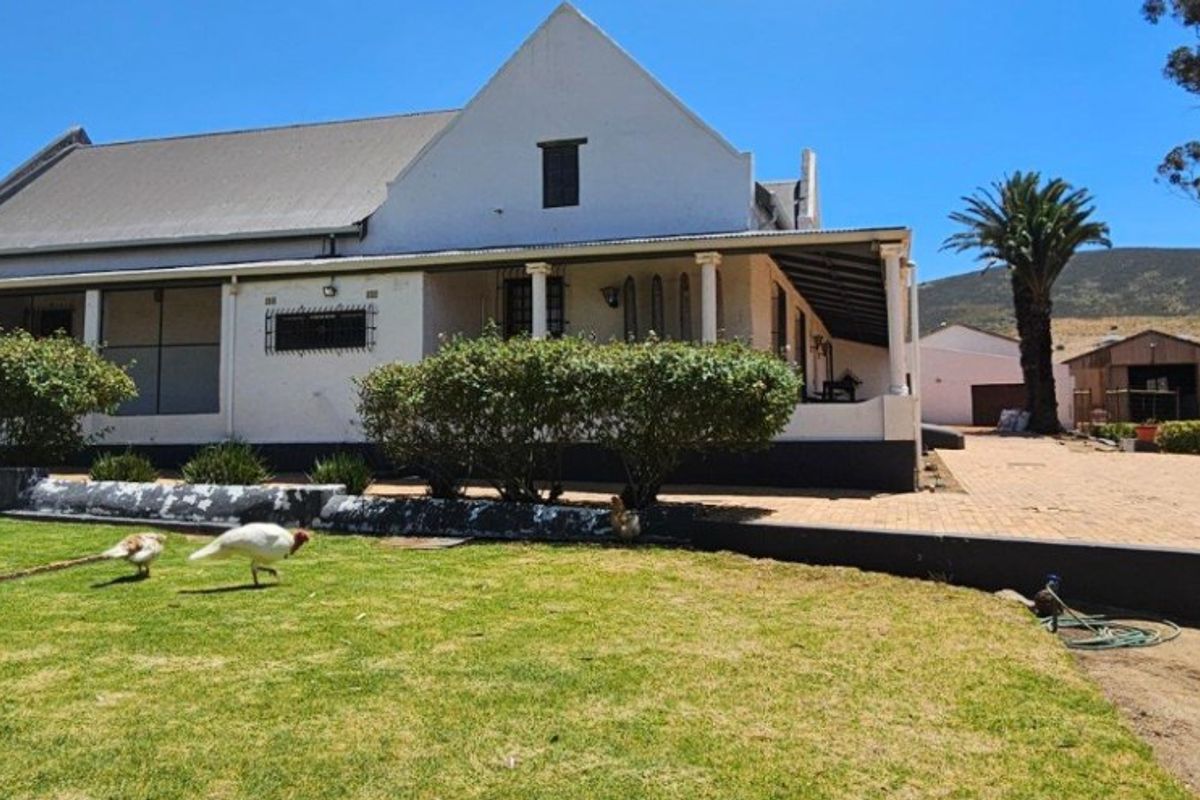 Rear view of a traditional farmhouse featuring a covered patio, gabled roof architecture, and a spacious garden area with an adjacent outbuilding.