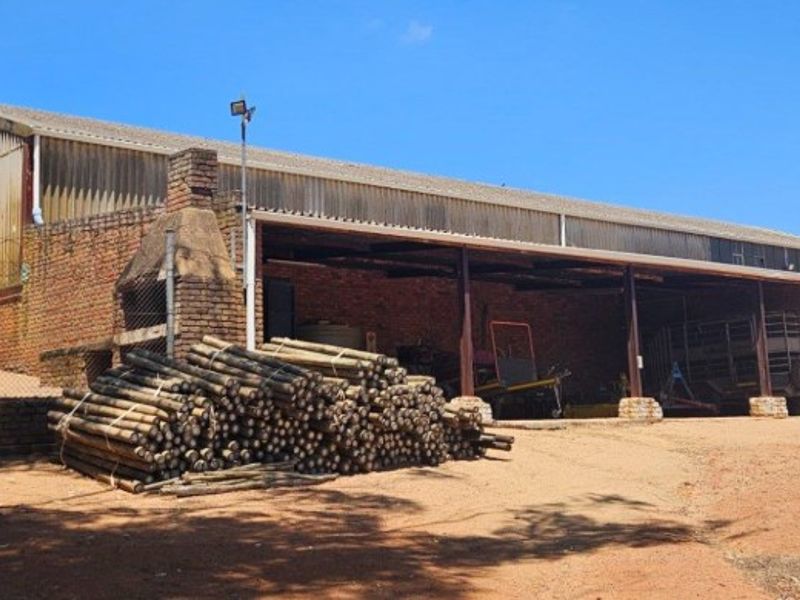 A large farm outbuilding featuring a covered storage area, brick masonry construction, and an integrated outdoor fireplace on the property grounds.