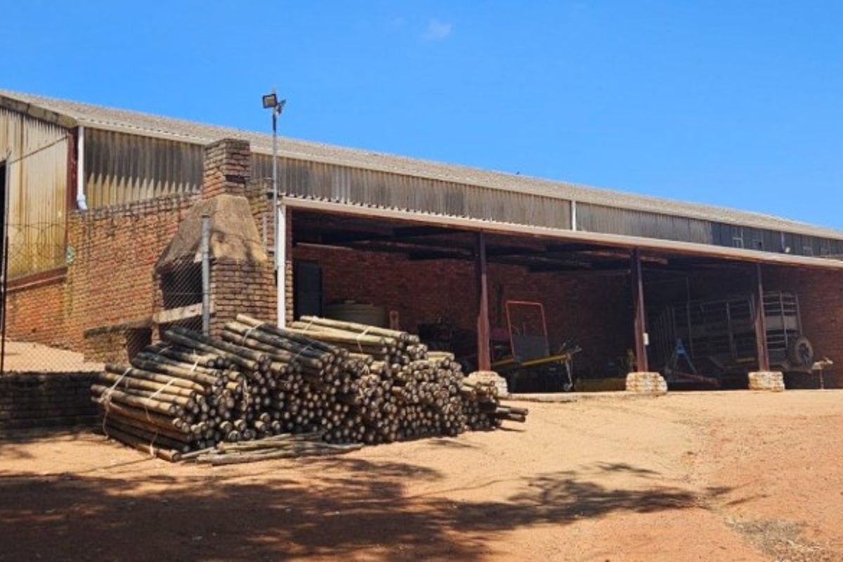 A large farm outbuilding featuring a covered storage area, brick masonry construction, and an integrated outdoor fireplace on the property grounds.