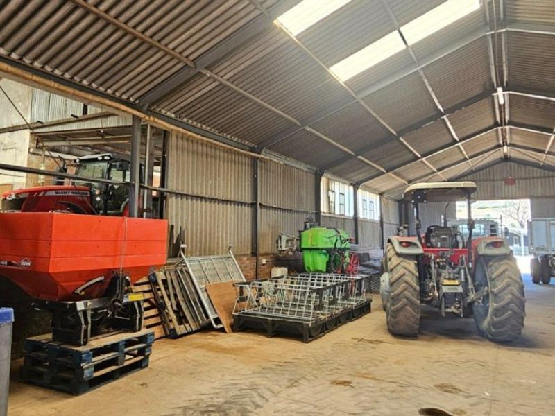 Spacious agricultural utility shed featuring a steel frame, corrugated metal roofing, skylights, and a durable concrete floor, suitable for machinery storage.