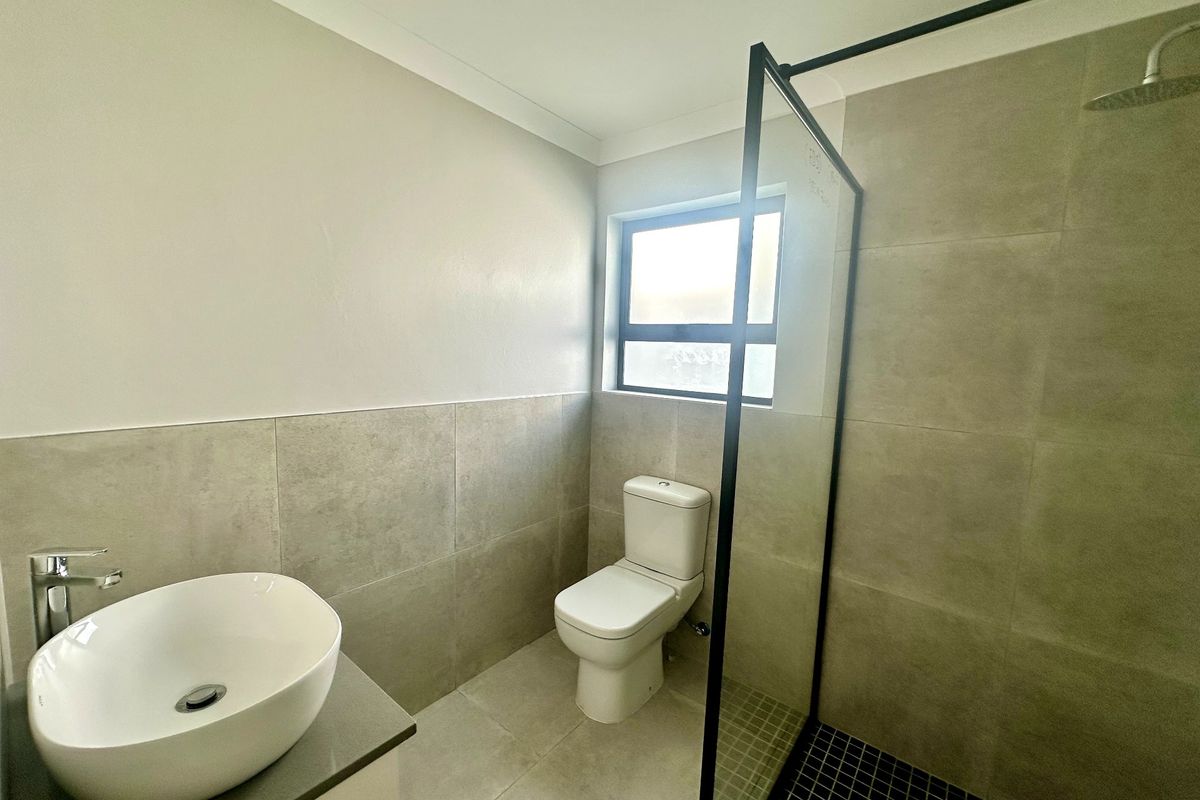 Modern bathroom featuring a vessel sink on a vanity, a toilet, and a spacious walk-in shower with a glass screen and rain shower head.