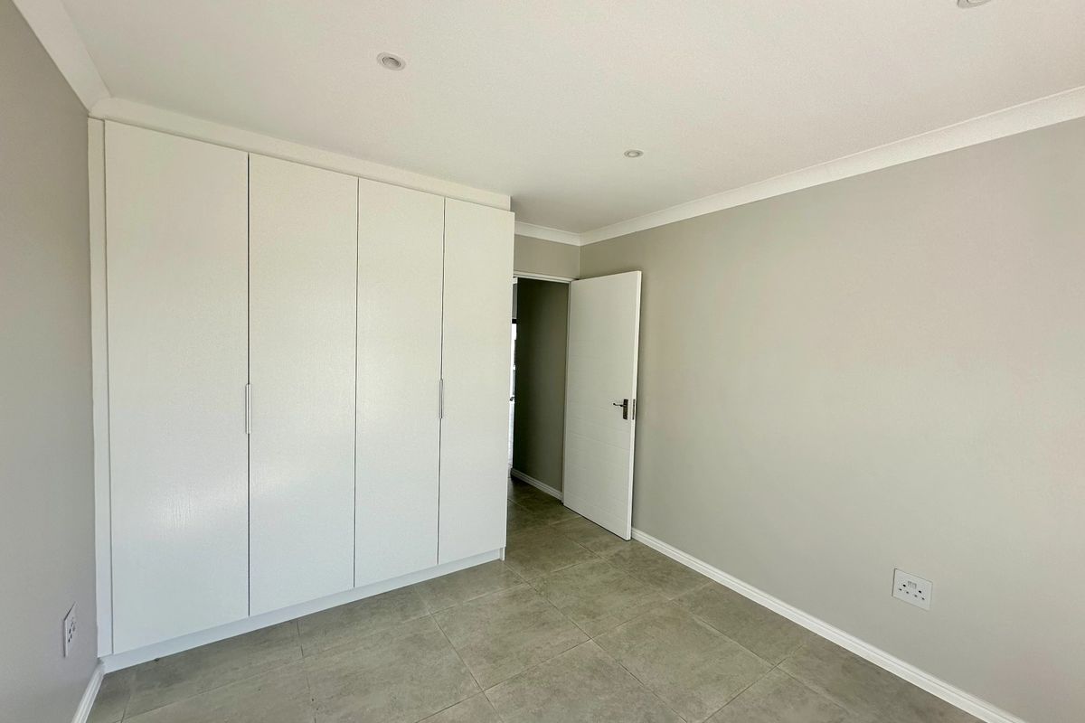 A clean, modern bedroom featuring neutral grey walls, tiled flooring, and ample built-in cupboard storage with recessed ceiling lighting.