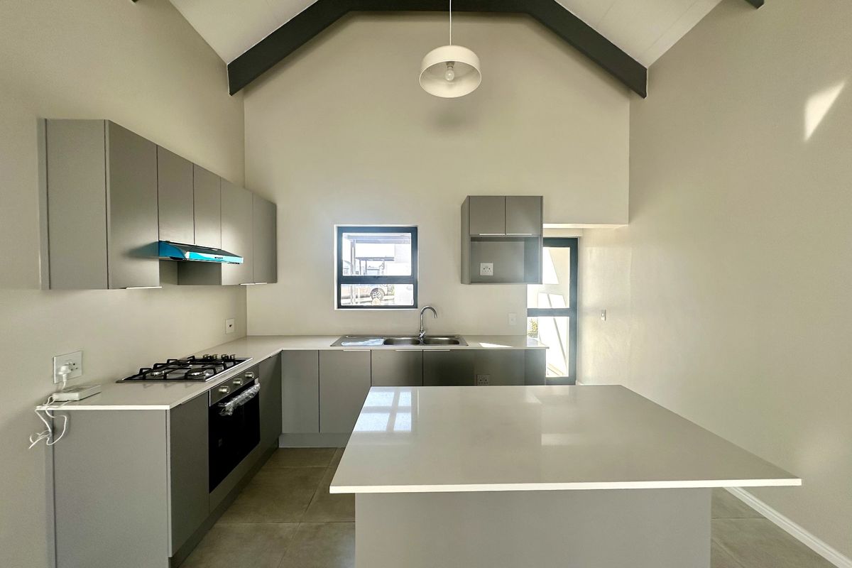 Modern kitchen featuring grey cabinetry, stone countertops, a central island, gas hob, and a striking vaulted ceiling with exposed beams.