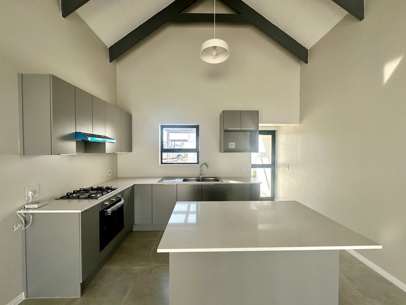 Modern kitchen featuring grey cabinetry, stone countertops, a central island, gas hob, and a striking vaulted ceiling with exposed beams.