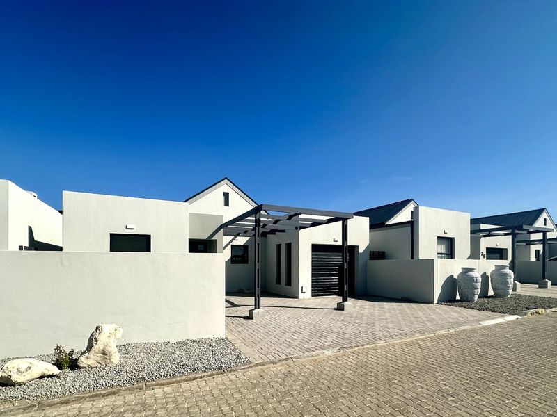 Modern residential facade featuring a paved driveway, clean architectural lines, and a structural pergola entrance.