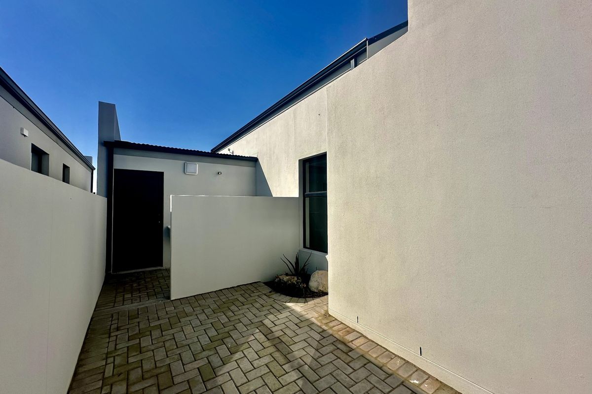 A clean and modern paved rear courtyard area featuring a private entrance door and high boundary walls.