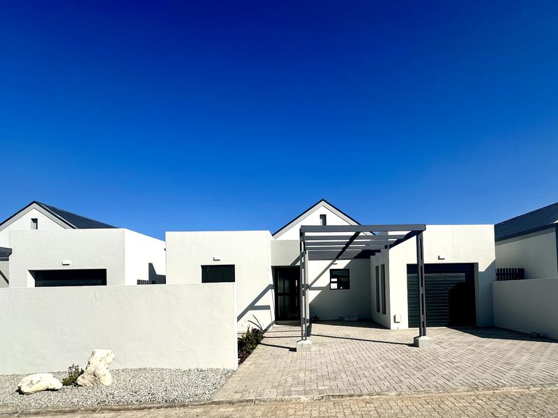 Modern single-story residential facade featuring a paved driveway, integrated garage, and a contemporary pergola structure under a clear blue sky.