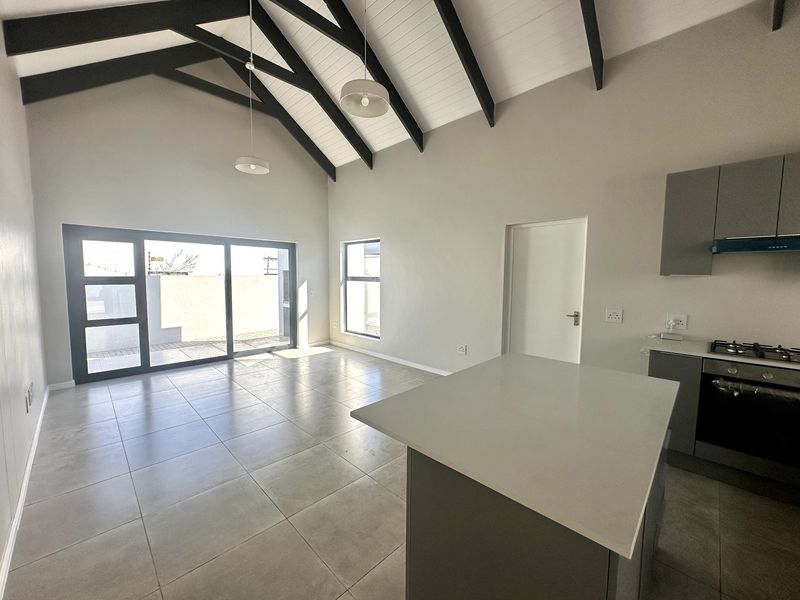 Spacious open-plan living area featuring a high vaulted ceiling with exposed beams, modern tiled floors, and a sleek kitchen with stone countertops.