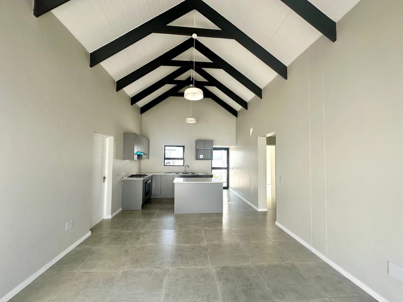 Spacious open-plan kitchen and living area featuring a high vaulted ceiling with exposed trusses, modern cabinetry, and neutral tiled flooring.