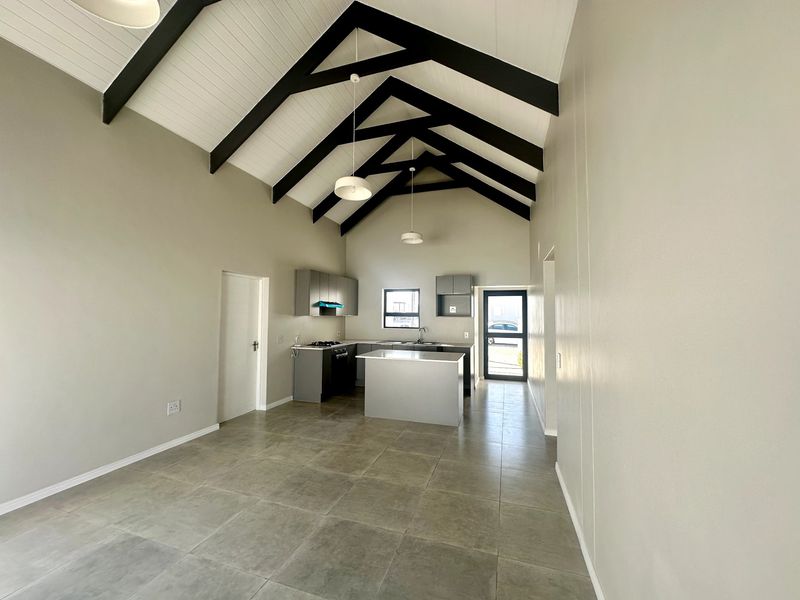 Spacious open-plan kitchen and living area featuring a high vaulted ceiling with exposed trusses, modern cabinetry, and neutral tiled flooring.