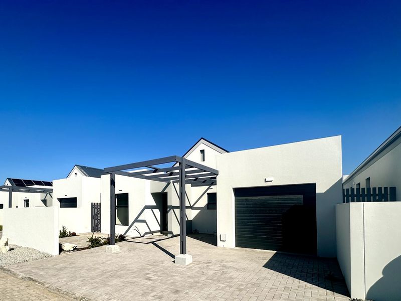 Modern single-story residential facade featuring a paved driveway, integrated garage, and a contemporary metal pergola structure.
