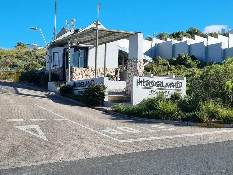 The entrance to Hoogland Estate featuring a paved driveway, security gatehouse, and perimeter wall.