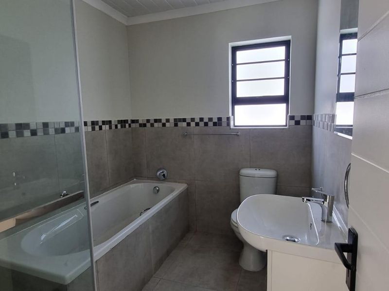 A clean, modern bathroom featuring a bathtub, separate shower enclosure, toilet, and vanity basin with neutral wall and floor tiling.