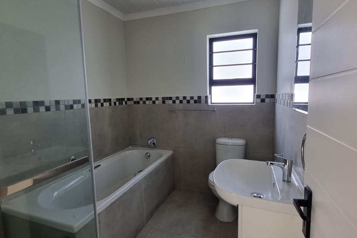 A clean, modern bathroom featuring a bathtub, separate shower enclosure, toilet, and vanity basin with neutral wall and floor tiling.