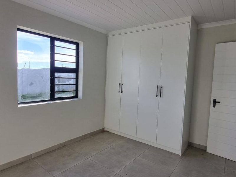 A clean, empty bedroom featuring neutral tiled flooring, built-in white cupboards, and a modern aluminium window frame.