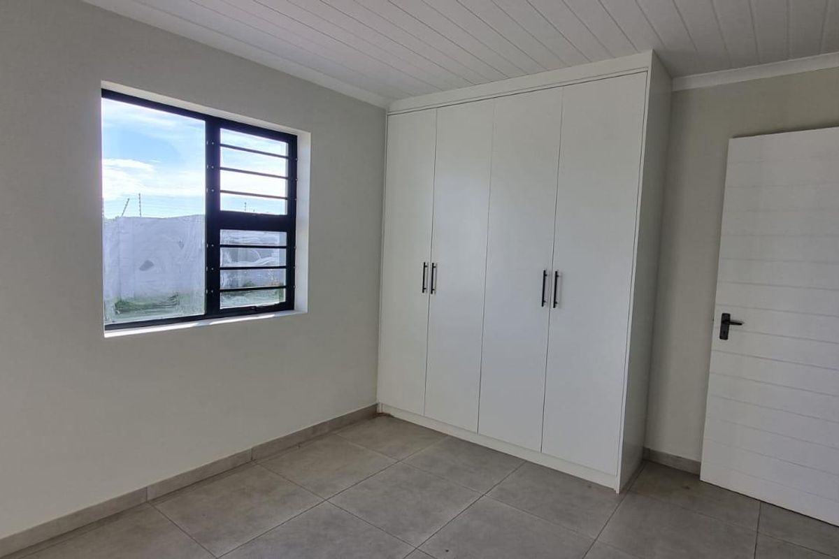 A clean, empty bedroom featuring neutral tiled flooring, built-in white cupboards, and a modern aluminium window frame.