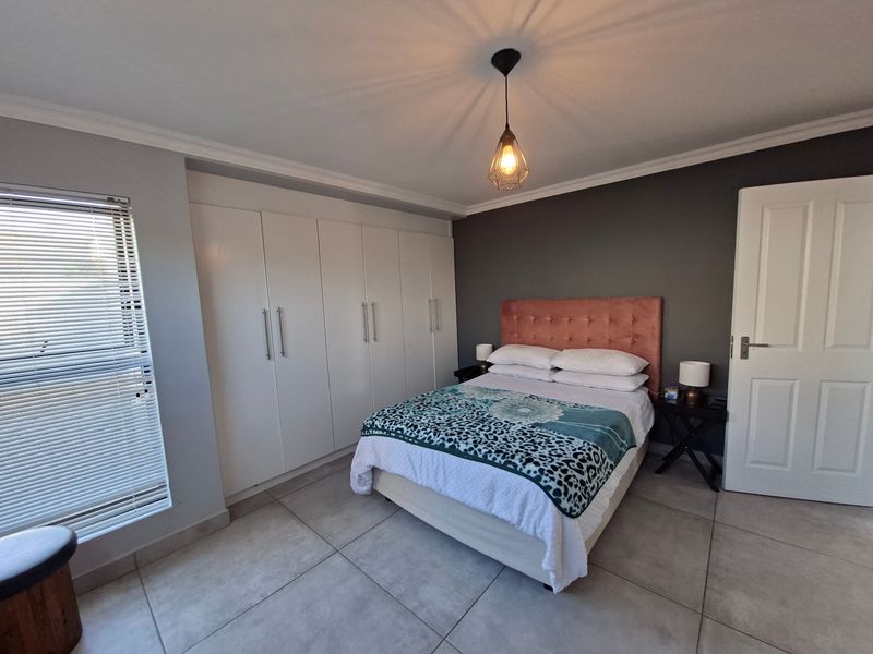 A well-maintained bedroom featuring neutral tiled flooring, built-in cupboards, and a modern pendant light fixture.