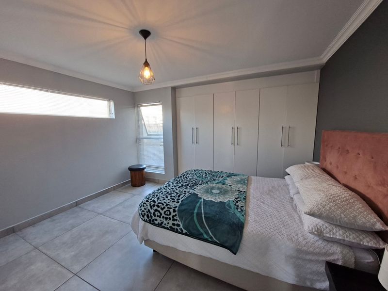 A well-maintained bedroom featuring neutral tiled flooring, built-in cupboards, and modern horizontal blinds, offering a clean and functional living space.