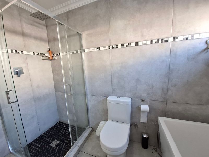 Modern bathroom featuring a glass-enclosed shower with rain head, mosaic floor tiling, a sleek dual-flush toilet, and a contemporary freestanding bathtub.
