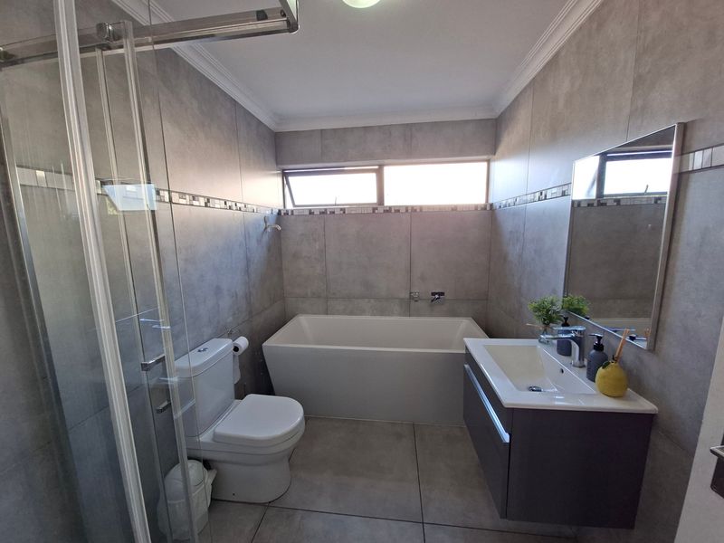 Modern bathroom featuring a sleek freestanding bathtub, glass-enclosed shower, wall-mounted vanity, and contemporary grey floor-to-ceiling tiling.
