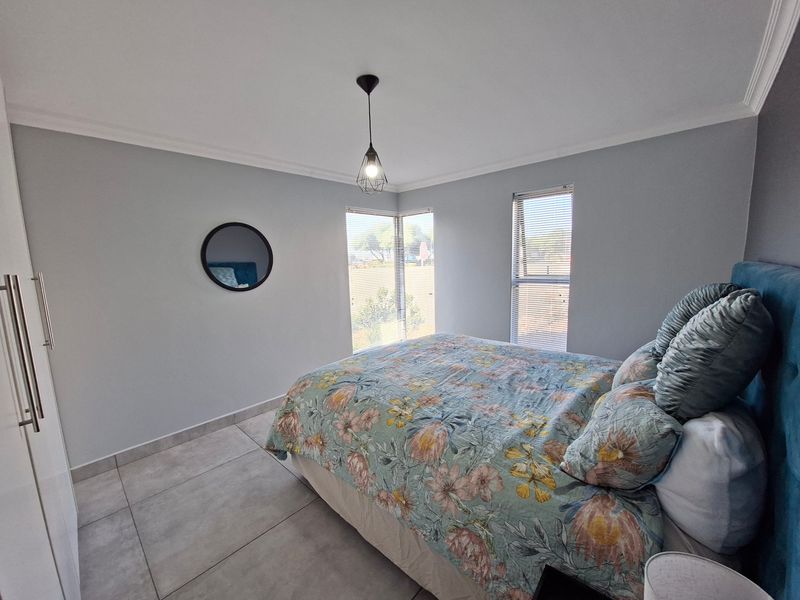 A bright bedroom featuring large corner windows with fitted blinds, neutral tiled flooring, and a built-in wardrobe.
