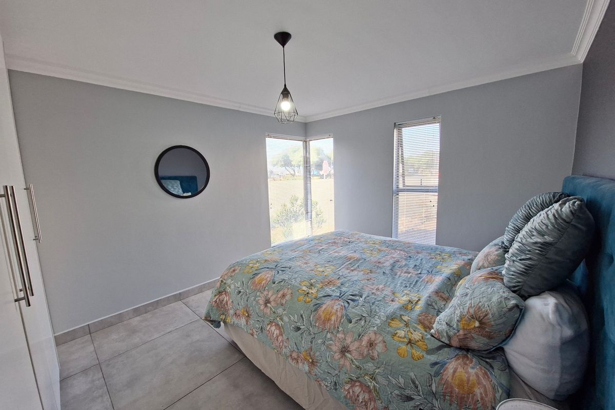 A bright bedroom featuring large corner windows with fitted blinds, neutral tiled flooring, and a built-in wardrobe.