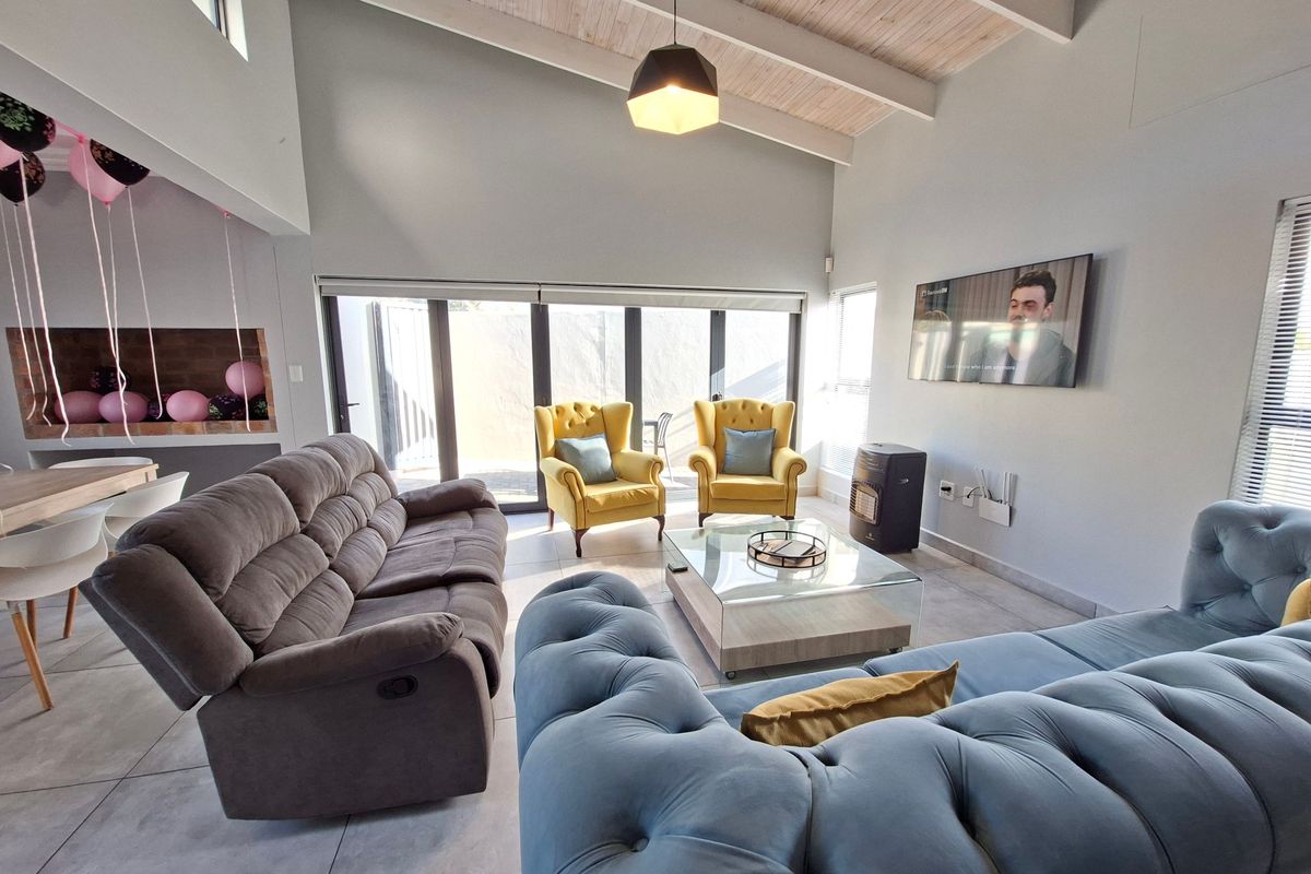 Spacious living room featuring a high vaulted timber ceiling, tiled floors, and large sliding glass doors that provide ample natural light.