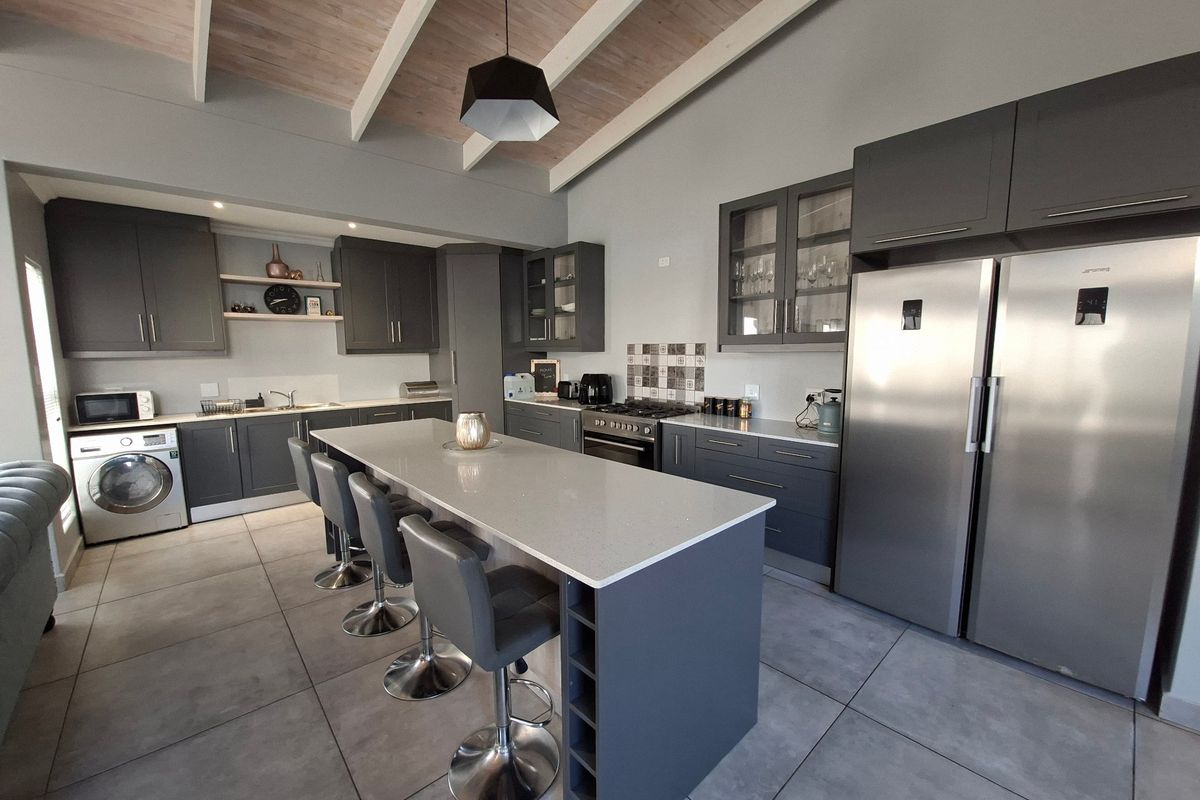 Modern kitchen featuring a large central island, quartz countertops, high-end stainless steel appliances, and an elegant exposed beam ceiling.