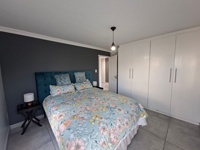 A well-maintained bedroom featuring neutral tiled flooring, built-in cupboards, and a modern pendant light fixture.