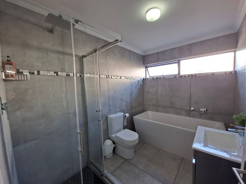 Modern bathroom featuring a walk-in shower with glass enclosure, a freestanding bathtub, a vanity with basin, and contemporary grey wall and floor tiling.