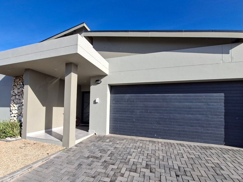 Modern front facade featuring a paved driveway, sectional garage door, covered entrance porch, and attractive stone cladding detail.