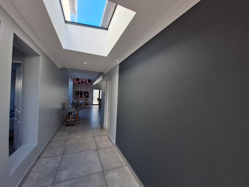 A bright, modern hallway featuring large format floor tiles, a prominent skylight, and clean, contemporary wall finishes.