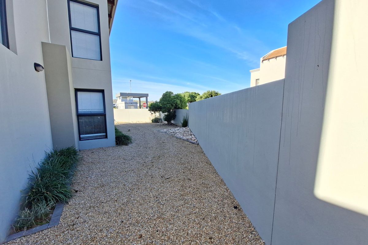 A side garden area featuring a gravel pathway, low-maintenance landscaping, and a high boundary wall providing privacy.