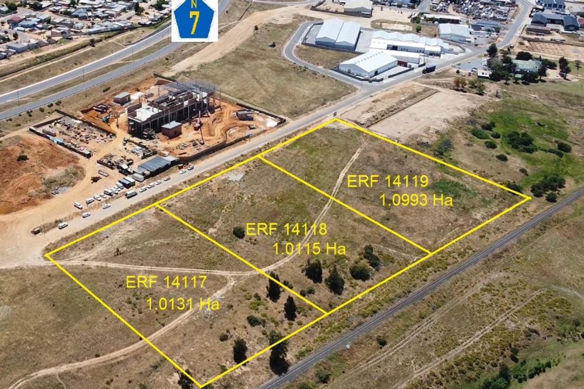 Aerial view of three adjacent vacant industrial land plots, clearly demarcated with boundary lines, situated near major road infrastructure.