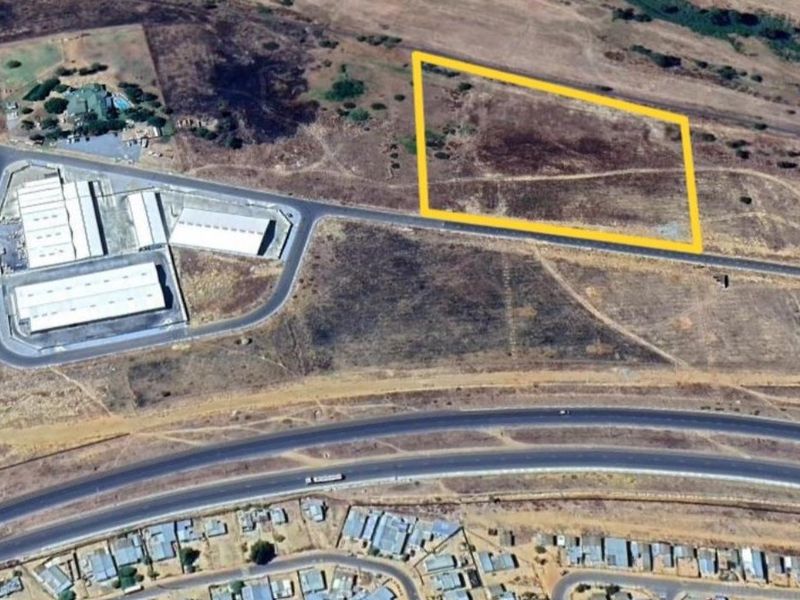 Aerial view of a vacant industrial plot with road access, situated near existing industrial facilities and major transport routes.