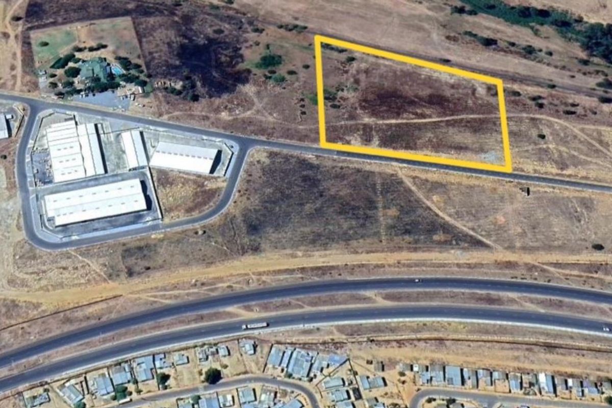 Aerial view of a vacant industrial plot with road access, situated near existing industrial facilities and major transport routes.