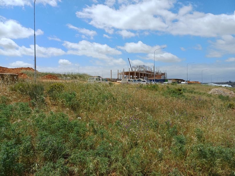 A view of an undeveloped industrial site with ongoing construction of a building structure in the background.
