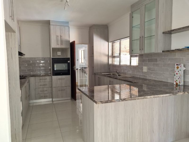 A modern, well-maintained kitchen featuring light wood-grain cabinetry, stone-look countertops, subway tile backsplash, and built-in oven, offering a clean and functional workspace.