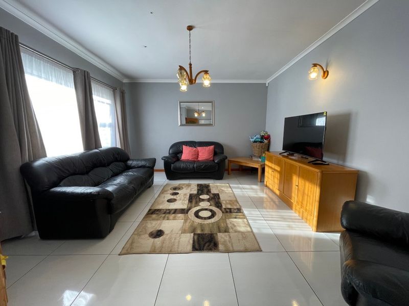 A spacious living room featuring large format floor tiles, neutral grey walls, and classic lighting fixtures, offering a clean and functional living space.