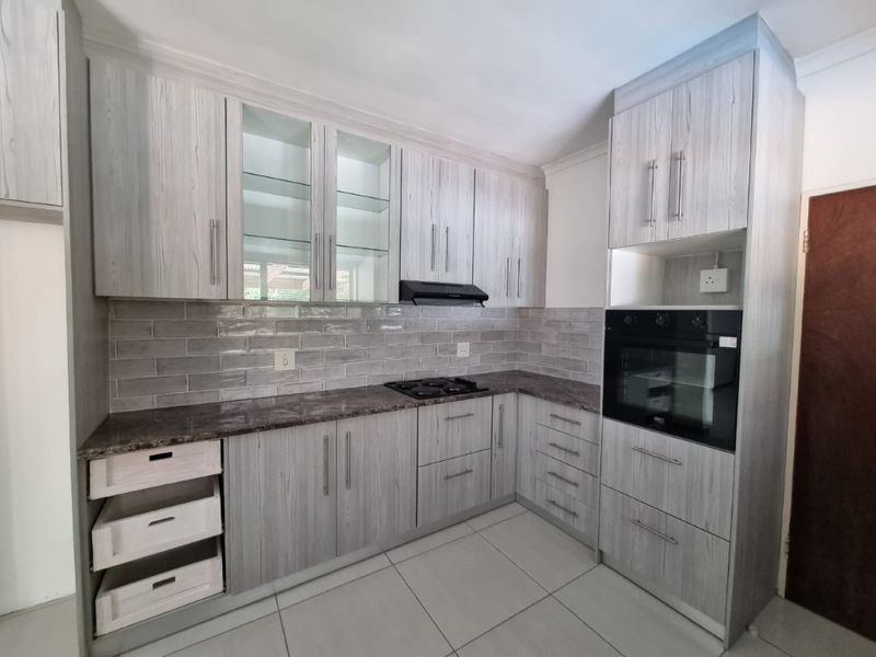Modern kitchen featuring light wood-grain cabinetry, stone countertops, subway tile backsplash, and integrated appliances including an oven and gas hob.