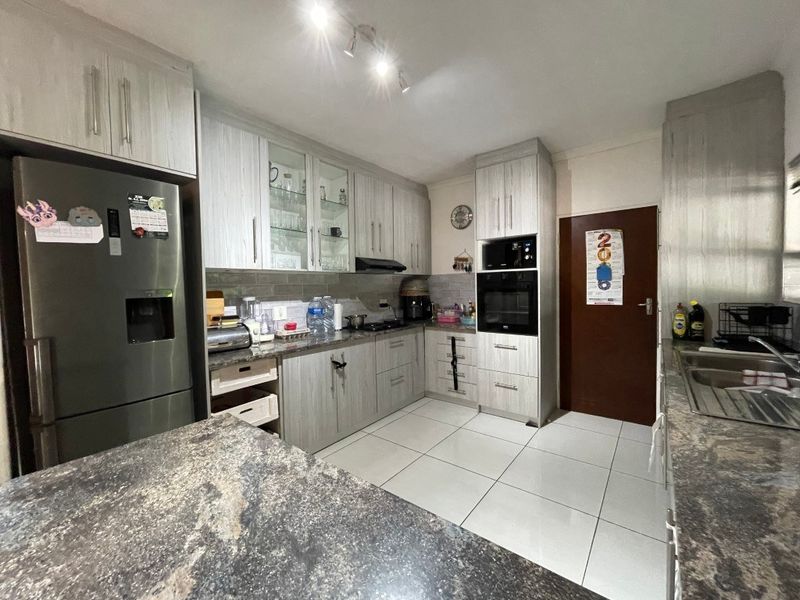 A well-maintained kitchen featuring granite countertops, built-in oven and microwave, extractor fan, and ample cabinetry with tiled flooring.